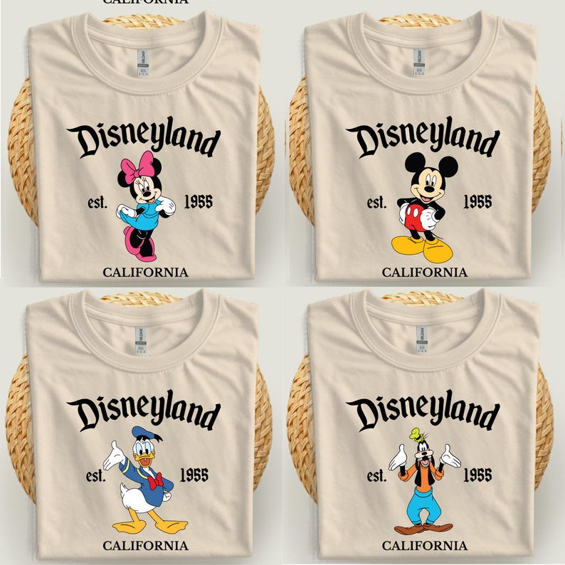 Op de afbeelding: Vier beige T-shirts met Disneyland-graphics. Elk shirt heeft een ander Disney-personage: Minnie Mouse, Mickey Mouse, Donald Duck en Goofy. De tekst "Disneyland est. 1955 CALIFORNIA" staat op elk shirt.