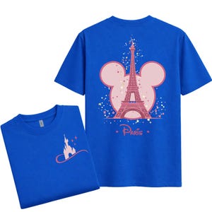 May include: Two blue t-shirts. One shirt features a pink Eiffel Tower design inside a Mickey Mouse head shape with the word "Paris". The other shirt has a pink castle design. Both shirts are short-sleeved.