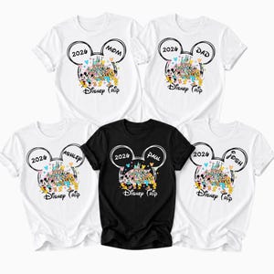 May include: A selection of white and black t-shirts with a Disney theme. Each shirt displays a Mickey Mouse ear design with the year "2026" and the names "Mom", "Dad", "Ashley", "Paul", and "Josh". The shirts also have a colourful Disney castle graphic and the words "Disney Trip".
