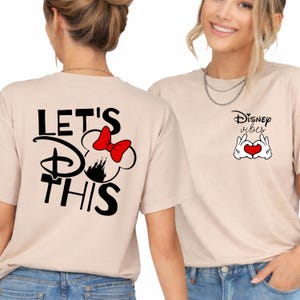 K&ouml;nnte beinhalten: Beige T-Shirts mit Disney-Motiven. Ein Shirt zeigt "LET'S DO THIS" mit einem Minnie Mouse-Design und einer roten Schleife. Das andere Shirt zeigt "Disney Vibes" mit einem Handherz-Symbol und einem roten Herzen.