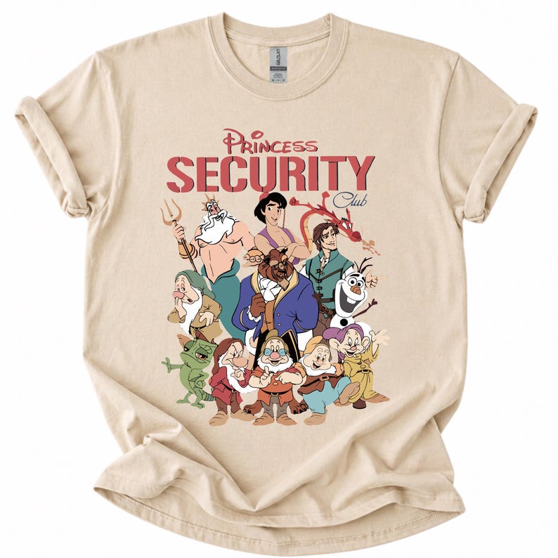 May include: Beige t-shirt with a graphic of cartoon characters and the text "Princess Security Club" in red. The design includes characters such as Ariel, Beast, and Olaf. The shirt is made of a soft material.