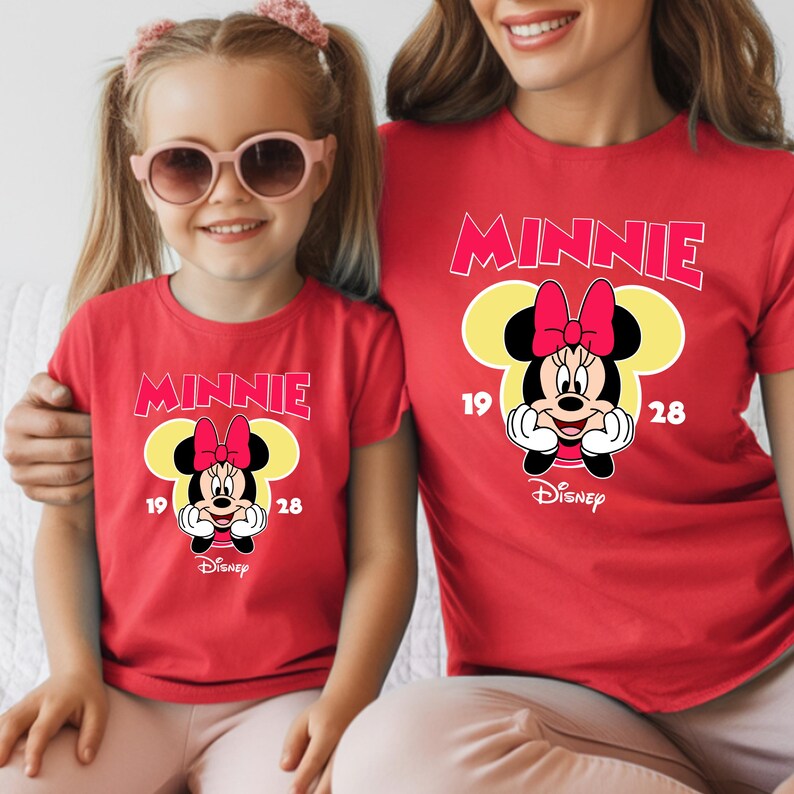 May include: Red t-shirts featuring a Minnie Mouse graphic. The design includes the word "MINNIE" in pink, a yellow Mickey Mouse head shape, and a Minnie Mouse character with a pink bow. The Disney logo is also visible.