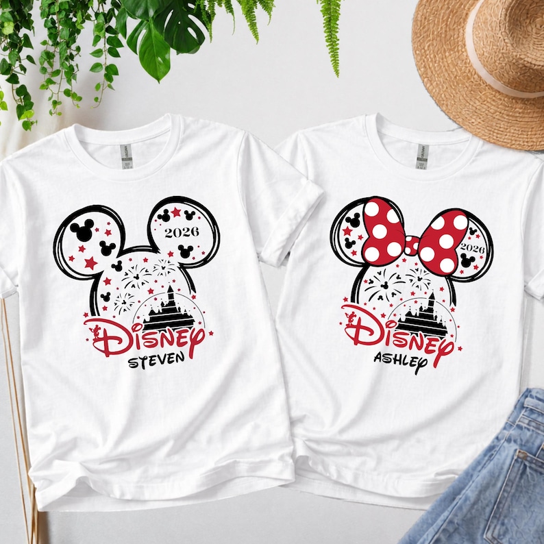 May include: Two white t-shirts with Disney designs. One has a Mickey Mouse head with red stars and the name "Steven", the other a Minnie Mouse bow with the name "Ashley". Both shirts include the year "2026".