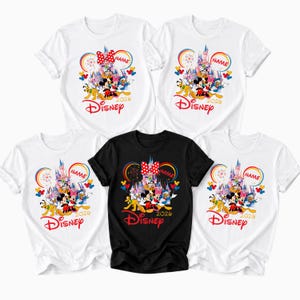 Op de afbeelding: Vijf T-shirts, vier witte en &eacute;&eacute;n zwarte, met een kleurrijk Disney-ontwerp. Het ontwerp toont een kasteel, Mickey Mouse en andere personages, samen met het woord "Disney" en het jaar "2024". Elk shirt heeft een aanpasbaar naamgebied.