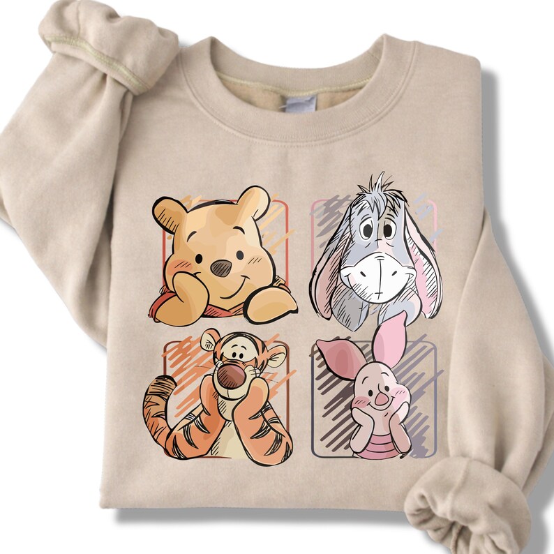 May include: Beige sweatshirt featuring four cartoon character portraits: Winnie the Pooh, Eeyore, Tigger, and Piglet. Each character is in a colored square. The sweatshirt has long sleeves and a crew neck.