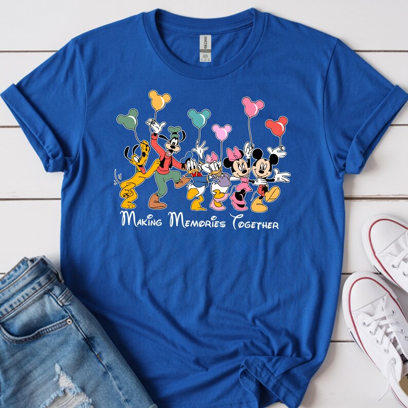 May include: A royal blue t-shirt featuring a graphic of Disney characters, including Mickey and Minnie Mouse, Pluto, Goofy, Donald and Daisy Duck, holding heart-shaped balloons. The text "Making Memories Together" is printed below the characters.
