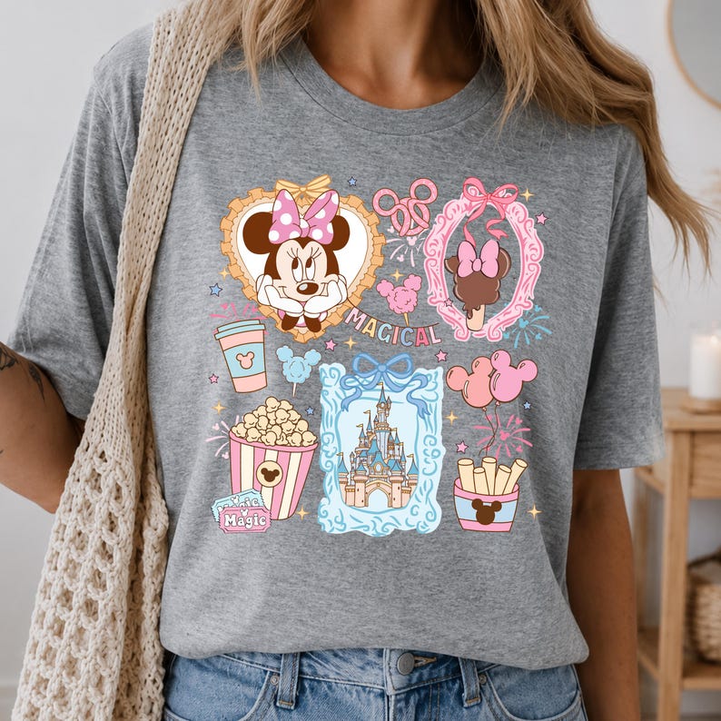 Puede incluir: Camiseta gris con un gr&aacute;fico colorido con Minnie Mouse, helado, palomitas de ma&iacute;z, un castillo y otras ilustraciones tem&aacute;ticas de Disney. La palabra "MAGICAL" tambi&eacute;n se muestra en la camiseta.
