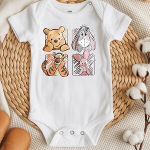 May include: White baby onesie featuring four cartoon character illustrations: Winnie the Pooh, Eeyore, Tigger, and Piglet. The illustrations are in individual rectangular frames with pastel color backgrounds. The onesie has short sleeves and snap closures.