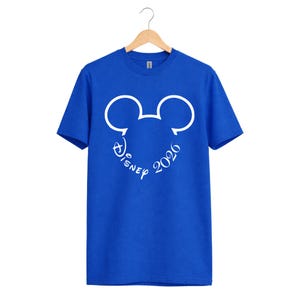 May include: Royal blue t-shirt featuring a white Mickey Mouse head outline with the word "Disney" and the year "2026" in a script font. The shirt is hanging on a wooden hanger.