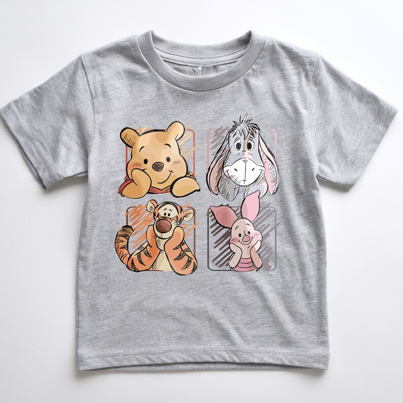 May include: A gray t-shirt featuring four cartoon character portraits: Winnie the Pooh, Eeyore, Tigger, and Piglet. The illustrations are in a sketched style, with each character in a separate square. The shirt is made of a soft, comfortable material.