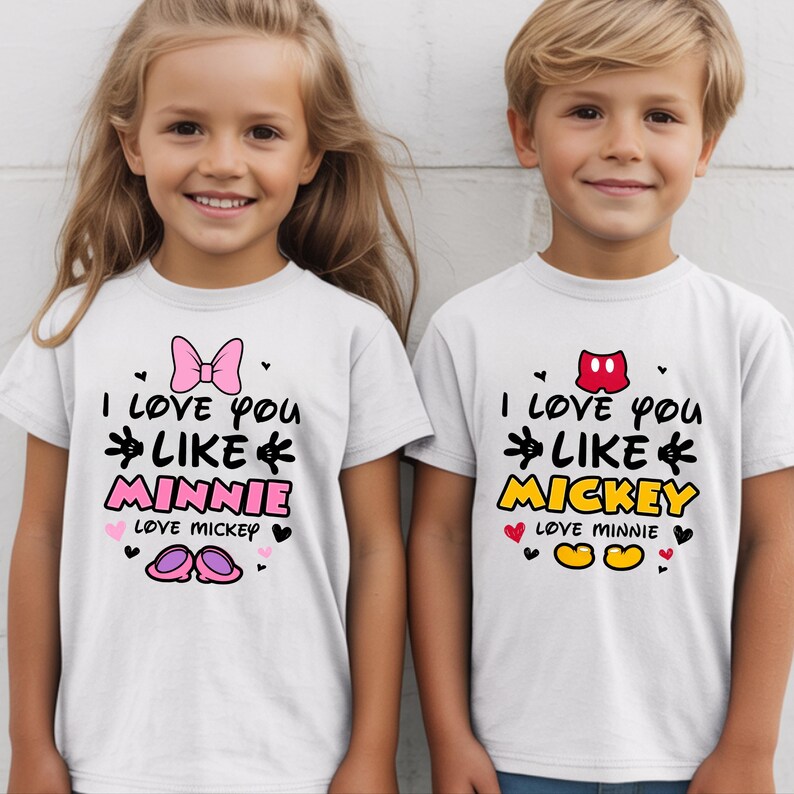 Pode incluir: Duas camisetas brancas com o texto "I love you like Minnie" e "I love you like Mickey" em preto, rosa e amarelo. A camiseta da Minnie tem um la&ccedil;o rosa, e a camiseta do Mickey tem um gr&aacute;fico vermelho do Mickey Mouse.
