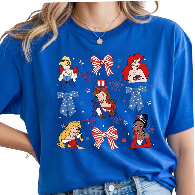 May include: A royal blue t-shirt with a patriotic design. It features cartoon princesses, bows, and fireworks in red, white, and blue. The design includes stars and bow ties, creating a festive look.