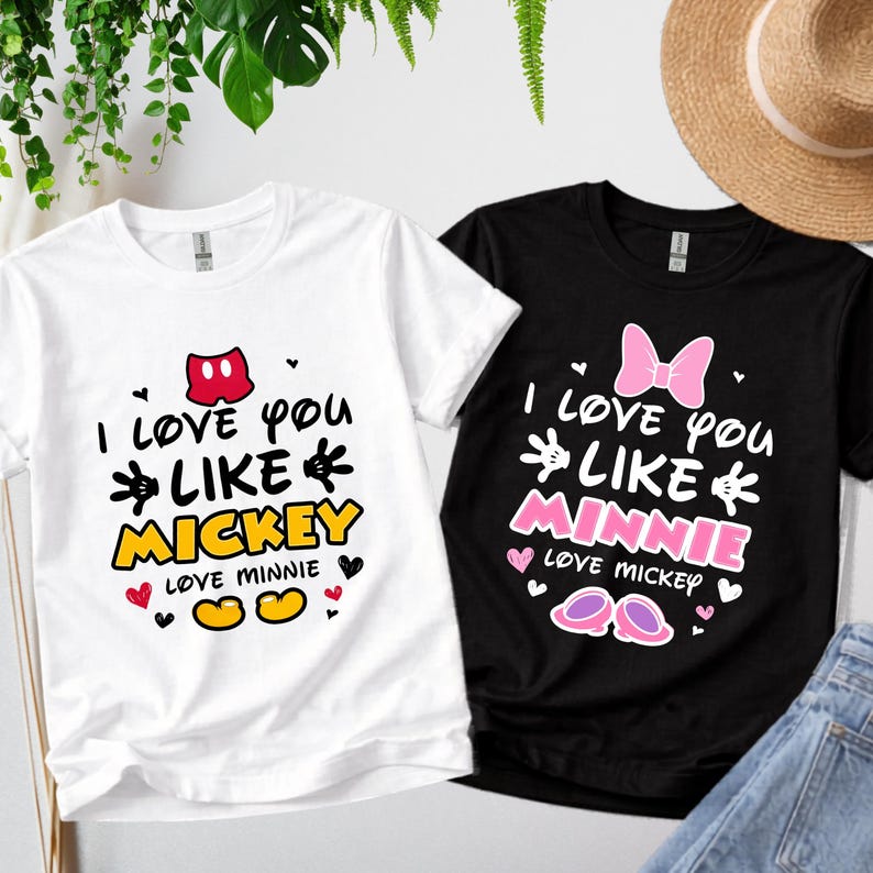 Pode incluir: Duas camisetas, uma branca e outra preta, com gr&aacute;ficos tem&aacute;ticos da Disney. A camiseta branca diz "I love you like Mickey" e a camiseta preta diz "I love you like Minnie". Ambas as camisetas t&ecirc;m cora&ccedil;&otilde;es e designs inspirados no Mickey Mouse.