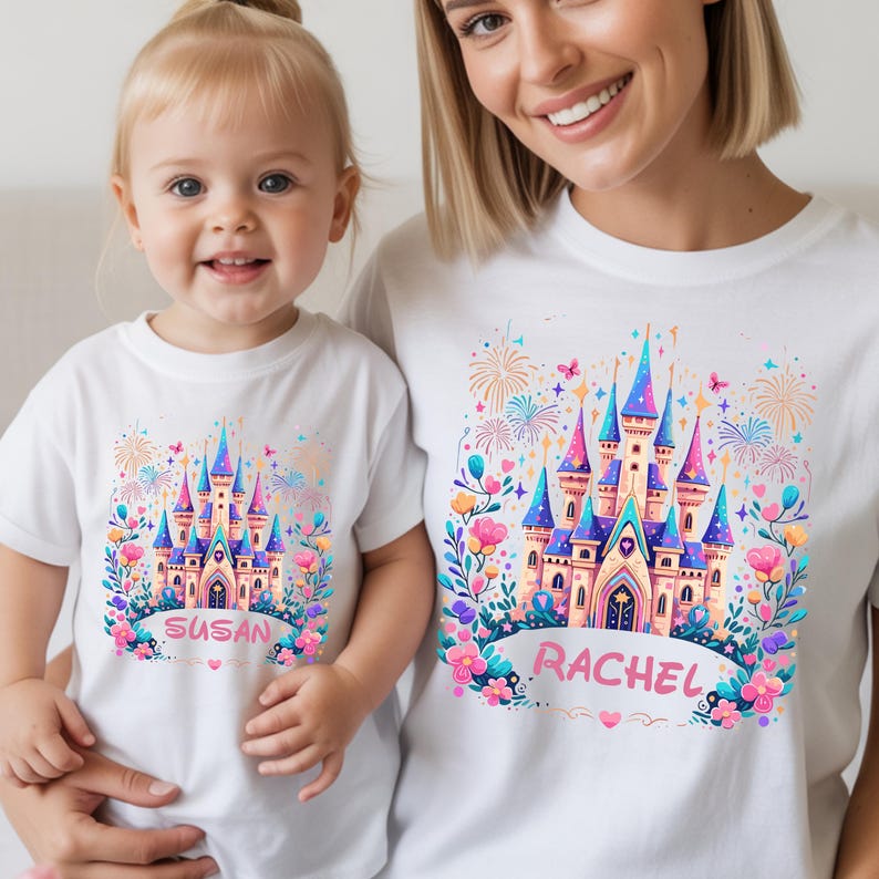 K&ouml;nnte beinhalten: Wei&szlig;e T-Shirts mit einem farbenfrohen Schlossmotiv. Das Schloss hat blaue, rosa und lila T&uuml;rme, umgeben von Blumen und Feuerwerk. Ein Shirt zeigt "SUSAN", das andere "RACHEL".
