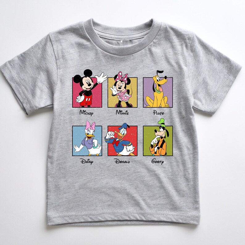 May include: A gray t-shirt featuring six Disney characters: Mickey Mouse, Minnie Mouse, Pluto, Daisy Duck, Donald Duck, and Goofy. Each character is in a colorful square with their name below. The shirt is made of a soft material.