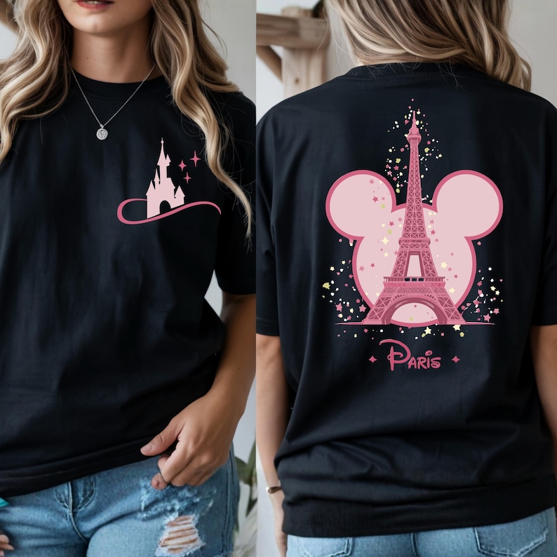 May include: Black t-shirt featuring a pink castle graphic on the front and a pink Eiffel Tower design with the word "Paris" on the back. The design incorporates a Mickey Mouse silhouette.