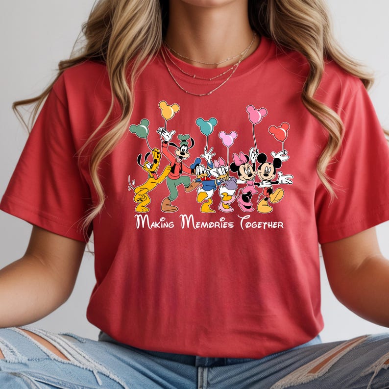 May include: Red t-shirt featuring a graphic of Disney characters including Mickey Mouse, Minnie Mouse, Donald Duck, and Goofy, holding balloons. The text "Making Memories Together" is printed below the characters.