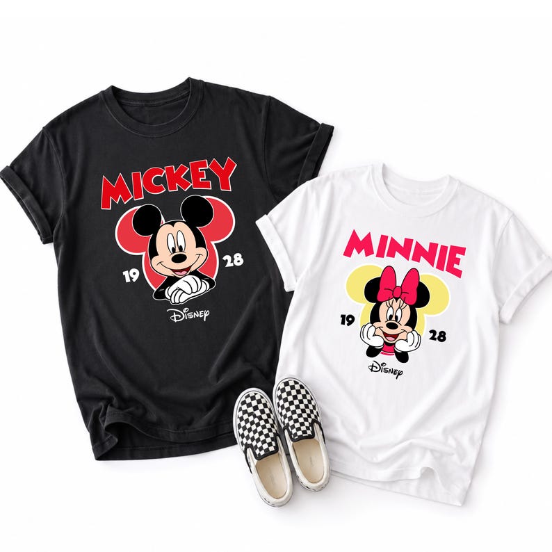 May include: Two t-shirts, one black and one white, featuring Mickey and Minnie Mouse designs. The black shirt has "Mickey" in red, and the white shirt has "Minnie" in pink. Both shirts have the Disney logo and the numbers "19" and "28".