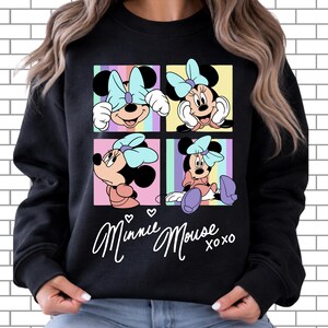 Pu&ograve; includere: Felpa nera con quattro pannelli che mostrano illustrazioni di Minnie Mouse. Ogni pannello mostra una posa diversa di Minnie Mouse con un fiocco azzurro. Le parole "Minnie Mouse xoxo" sono scritte in bianco sotto i pannelli.