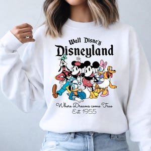 Pu&ograve; includere: Felpa bianca con la scritta "Walt Disney's Disneyland" e una grafica di Topolino, Minnie, Paperino, Pippo, Paperina e Pluto. Sotto, la scritta "Where Dreams come True Est. 1955". Un classico design Disney.