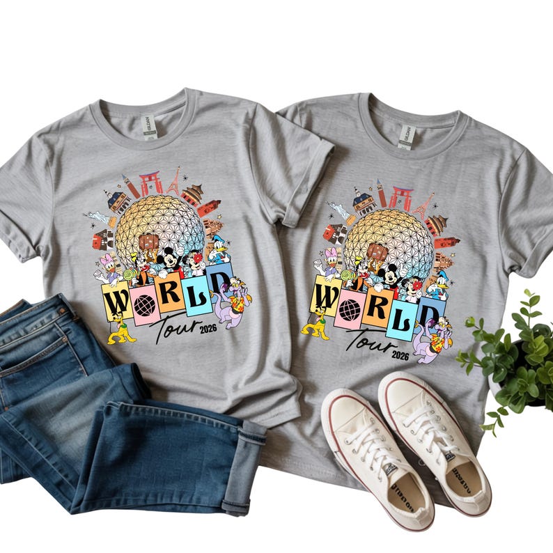 May include: Two grey t-shirts with a colourful graphic featuring Disney characters, a globe, and the text "WORLD Tour 2026." The shirts are paired with blue jeans and white canvas trainers.