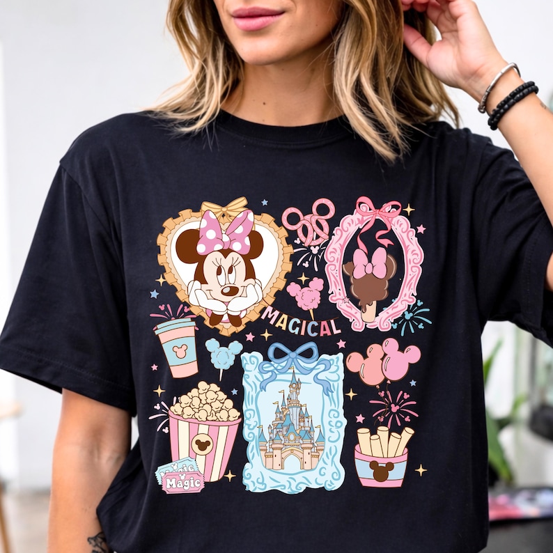 Puede incluir: Camiseta negra con un gr&aacute;fico colorido con Minnie Mouse, un castillo, palomitas de ma&iacute;z y otros elementos tem&aacute;ticos. La palabra "MAGICAL" tambi&eacute;n se muestra. El dise&ntilde;o incluye detalles en rosa, azul y dorado.