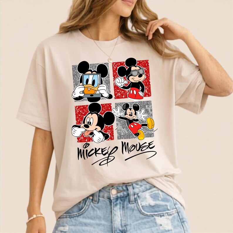 Op de afbeelding: Beige T-shirt met een vierpaneelsafbeelding van Mickey Mouse en Donald Duck. Elk paneel toont een andere pose van Mickey Mouse en Donald Duck. De woorden "Mickey Mouse" staan eronder in cursieve letters.