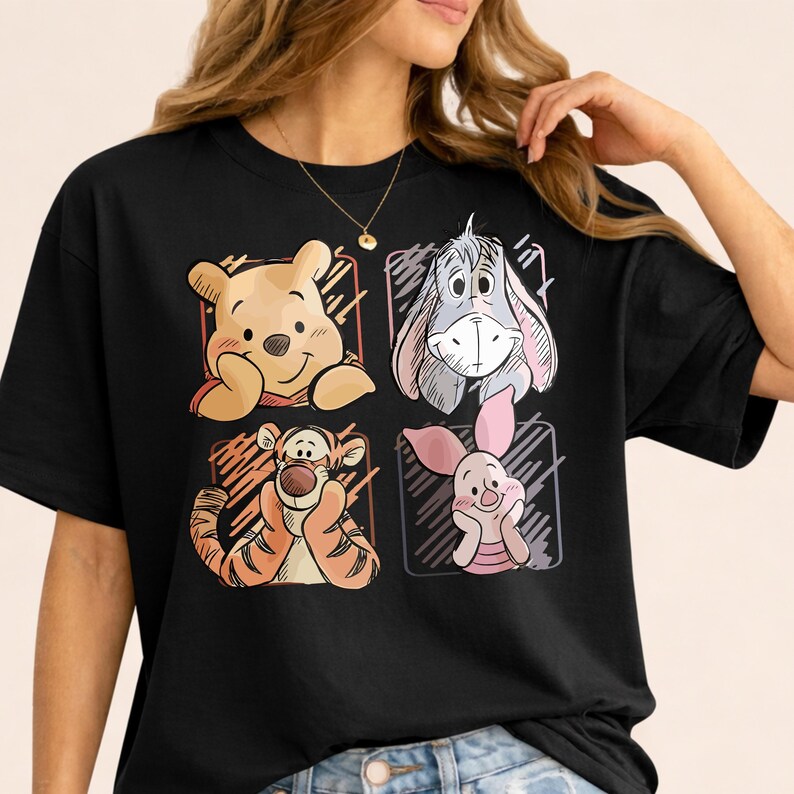 May include: Black t-shirt featuring four cartoon character portraits: Winnie the Pooh, Eeyore, Tigger, and Piglet. Each character is in a square frame with a sketched design. The shirt is a classic crew neck style.