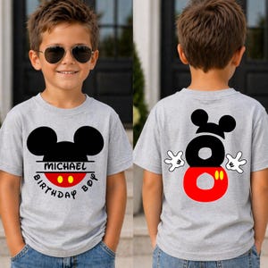 May include: A gray t-shirt featuring a black Mickey Mouse head design with the name "MICHAEL" and "BIRTHDAY BOY" printed on the front. The back of the shirt displays a large number "8" with Mickey Mouse hands.