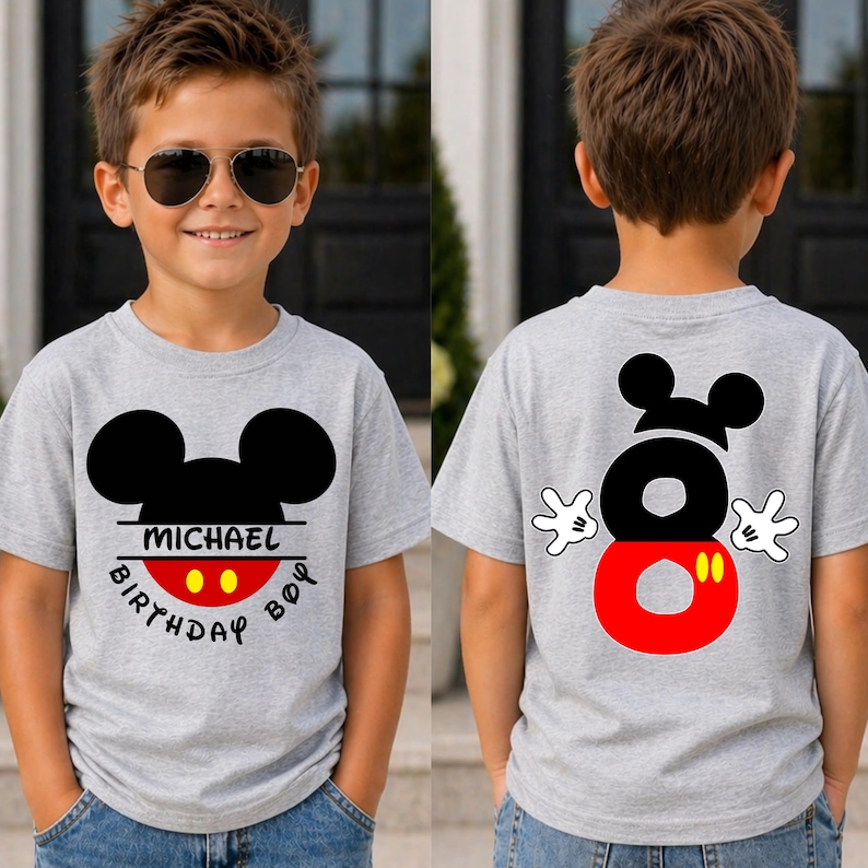 May include: A gray t-shirt featuring a black Mickey Mouse head design with the name "MICHAEL" and "BIRTHDAY BOY" printed on the front. The back of the shirt displays a large number "8" with Mickey Mouse hands.