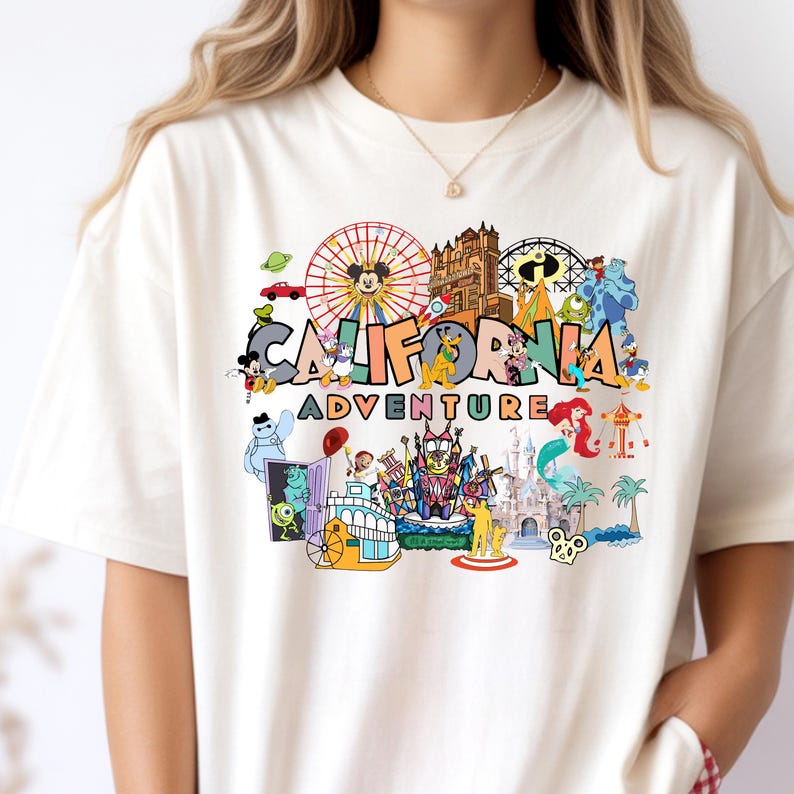 May include: A cream-coloured t-shirt with a vibrant graphic. The design features the words "CALIFORNIA ADVENTURE" alongside illustrations of a Ferris wheel, cartoon characters, and a castle, reminiscent of a theme park.