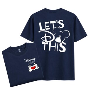 K&ouml;nnte beinhalten: Zwei marineblaue T-Shirts. Ein Shirt hat "Disney vibes" mit Mickey Mouse-H&auml;nden, die ein Herz formen. Das andere Shirt hat "Let's do this" mit einer Mickey Mouse-Kopf-Silhouette und dem Disney-Logo. Beide Shirts sind kurz&auml;rmelig.