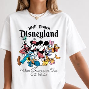 Pu&ograve; includere: T-shirt bianco con grafica Disney con Topolino, Minnie, Paperino, Pippo e Pluto. La maglietta mostra "Walt Disney's Disneyland", "Where Dreams come True Est. 1955". Un design classico.
