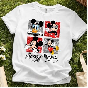 Op de afbeelding: Wit T-shirt met een ontwerp van vier panelen met Mickey Mouse in verschillende poses. De panelen wisselen af met rode en zilveren achtergronden. De woorden "Mickey Mouse" staan in een gestileerd lettertype eronder.