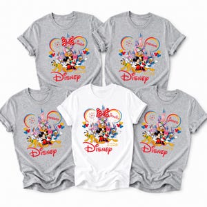 Op de afbeelding: Vijf shirts met korte mouwen, vier grijze en &eacute;&eacute;n witte, met een Disney-thema. Elk shirt heeft een kleurrijke afbeelding van Disney-personages, een kasteel en het Disney-logo. Namen staan boven de Mickey Mouse oren.
