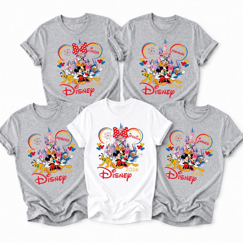 Op de afbeelding: Vijf shirts met korte mouwen, vier grijze en &eacute;&eacute;n witte, met een Disney-thema. Elk shirt heeft een kleurrijke afbeelding van Disney-personages, een kasteel en het Disney-logo. Namen staan boven de Mickey Mouse oren.