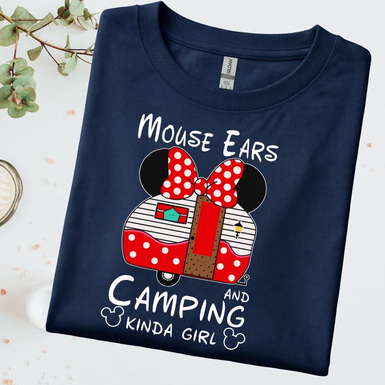 Puede incluir: Camiseta azul marino con un gr&aacute;fico de caravana de orejas de Minnie Mouse y el texto "Mouse Ears Camping Kinda Girl". La caravana tiene un lazo rojo de lunares y lunares y rayas rojos y blancos.