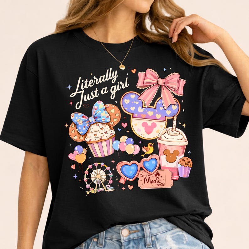 Pode incluir: Camiseta preta com um design gr&aacute;fico colorido com um cupcake, orelhas do Mickey, uma roda gigante, &oacute;culos de sol em forma de cora&ccedil;&atilde;o e uma bebida. O texto "Literally Just a girl" est&aacute; escrito em it&aacute;lico.