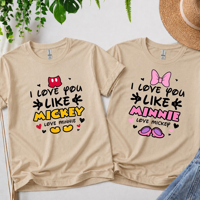 Pode incluir: Duas camisetas bege com os textos "I love you like Mickey" e "I love you like Minnie" em preto, amarelo e rosa. As camisetas apresentam gr&aacute;ficos de desenhos animados do Mickey e da Minnie.