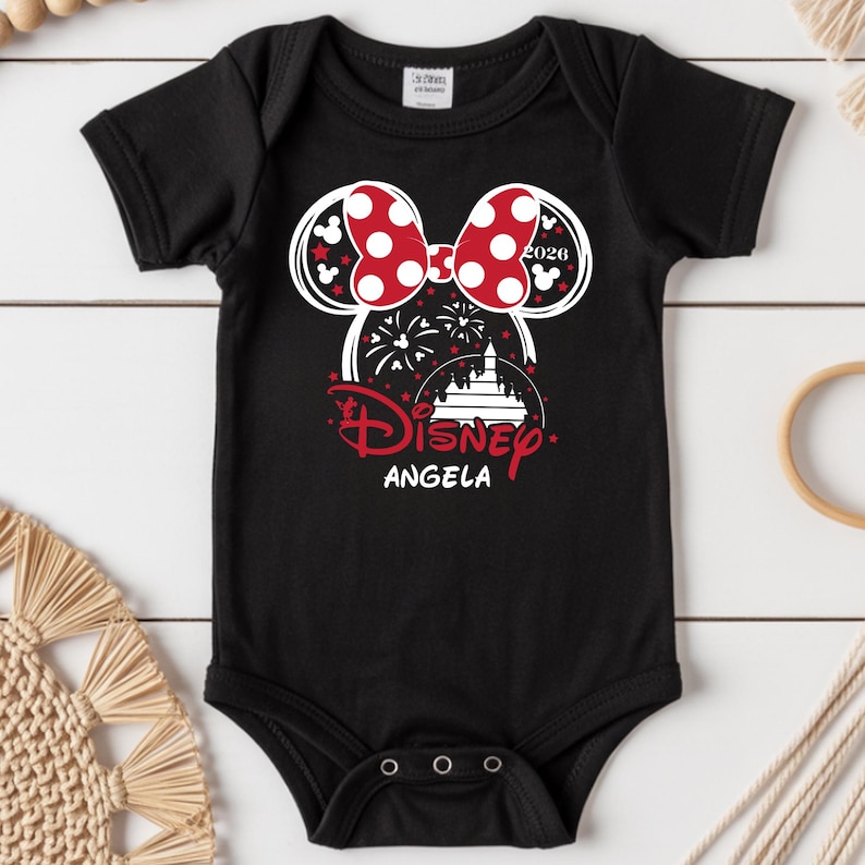 May include: Black baby bodysuit with a Minnie Mouse design. The design features a red polka dot bow, the word "Disney" in red script, and the name "Angela". The year "2020" is also included in the design.