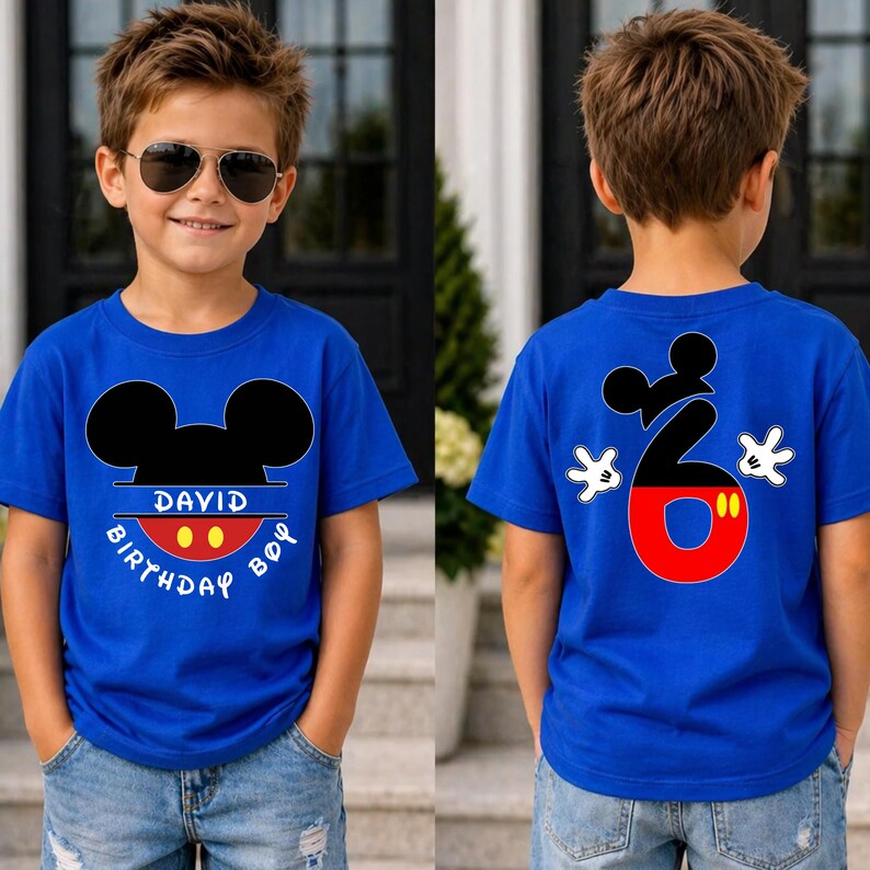 May include: A blue t-shirt with a Mickey Mouse design. The front of the shirt has Mickey's head and the words "DAVID BIRTHDAY BOY". The back of the shirt has a large number 6 with Mickey Mouse hands. The shirt is worn by a child.