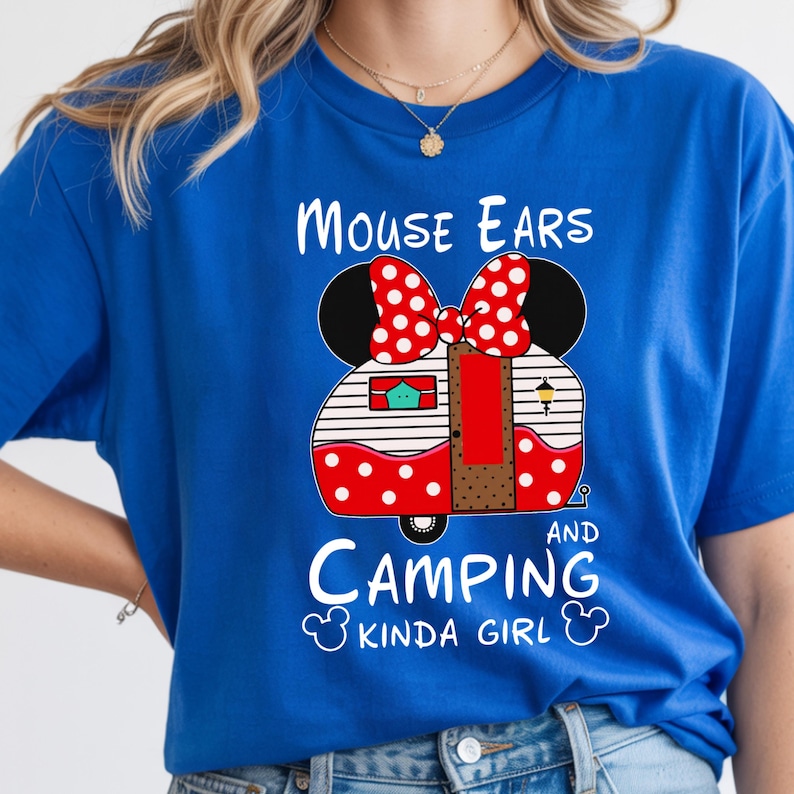 Puede incluir: Camiseta azul real con un dise&ntilde;o de caravana con forma de orejas de Minnie, un lazo rojo de lunares y el texto "MOUSE EARS AND CAMPING KINDA GIRL". La caravana tiene lunares rojos y rayas blancas.