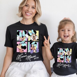 Pu&ograve; includere: T-shirt neri con una grafica colorata di Minnie Mouse. Il design include quattro pannelli con diverse pose di Minnie Mouse, un fiocco azzurro e la scritta "Minnie Mouse xoxo".