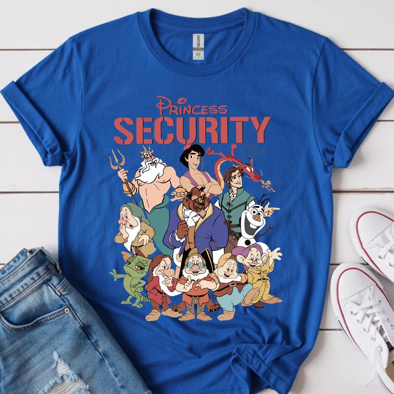 May include: Royal blue t-shirt with a graphic of cartoon characters and the text "Princess Security" in red. The characters include a mermaid, a beast, and dwarves. White trainers and blue jeans are in the background.