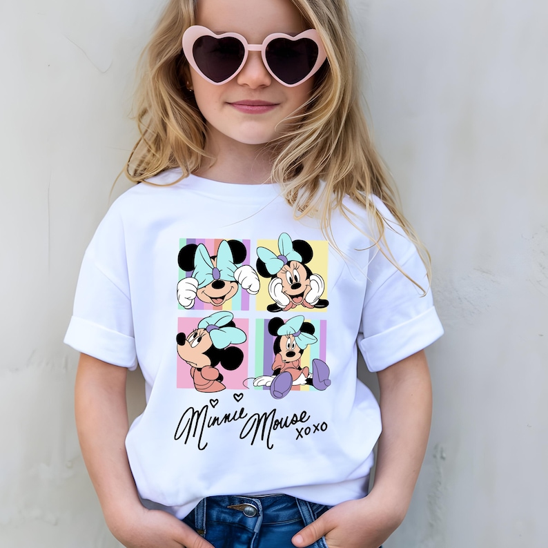 Pu&ograve; includere: T-shirt bianco con una grafica colorata di Minnie Mouse in quattro pose diverse, ciascuna in un quadrato. La maglietta ha le parole "Minnie Mouse xoxo" in corsivo. La ragazza indossa occhiali da sole a forma di cuore.