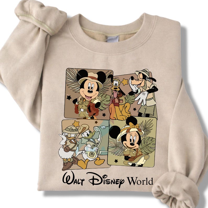Puede incluir: Sudadera beige con un gr&aacute;fico de Mickey Mouse, Pluto, Goofy, Donald Duck y Minnie Mouse con trajes de safari. Las palabras "Walt Disney World" est&aacute;n impresas en negro debajo. La sudadera tiene mangas largas.