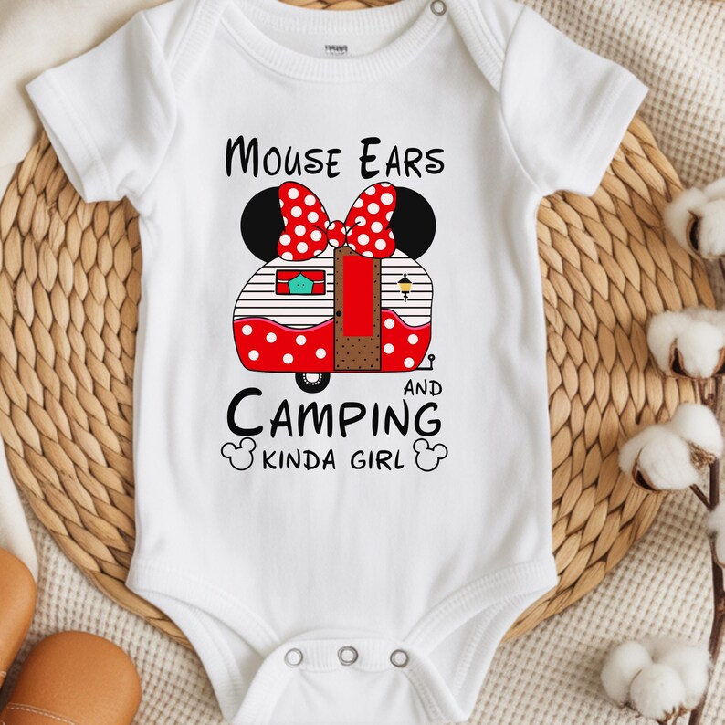 Puede incluir: Body de beb&eacute; blanco con un gr&aacute;fico de un lazo de lunares rojos y blancos y orejas de rat&oacute;n negras. El dise&ntilde;o incluye una caravana roja y blanca con el texto "MOUSE EARS AND CAMPING KINDA GIRL."