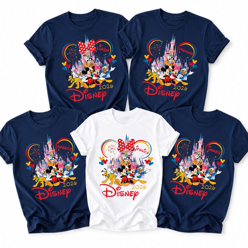 Op de afbeelding: Vijf marineblauwe en witte Disney T-shirts. Elk shirt heeft een kleurrijke afbeelding van Disney-personages, een kasteel en het woord "Disney" in het rood. De shirts hebben ook namen en het jaar 2020.