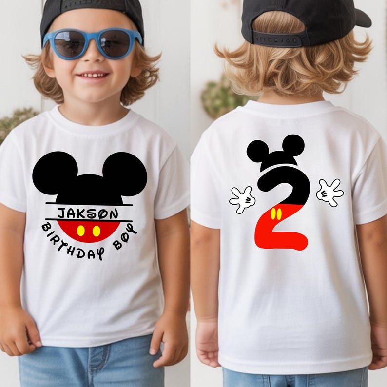 May include: White t-shirt featuring a black Mickey Mouse head design with the name "Jakson" and the words "Birthday Boy" on the front. The back of the shirt displays a large number "2" in black and red, with Mickey Mouse hands on either side.