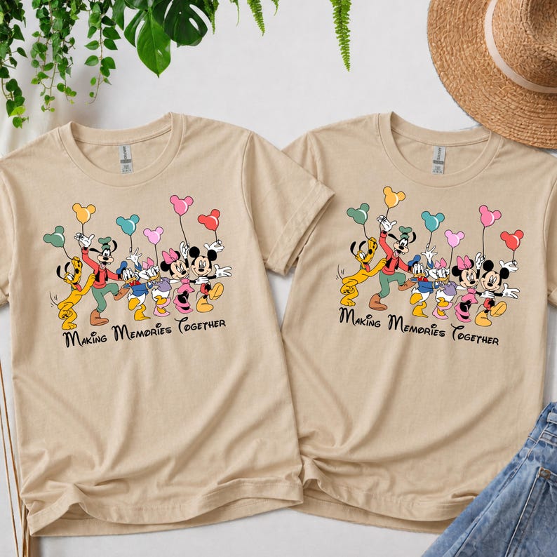 May include: Two beige t-shirts with a colorful graphic of Disney characters holding balloons. The characters include Mickey and Minnie Mouse, Donald and Daisy Duck, Goofy, and Pluto. The text "Making Memories Together" is printed below the characters.